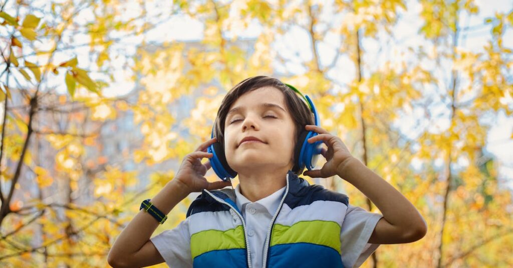 A young boy enjoys music through headphones amidst colorful fall foliage.